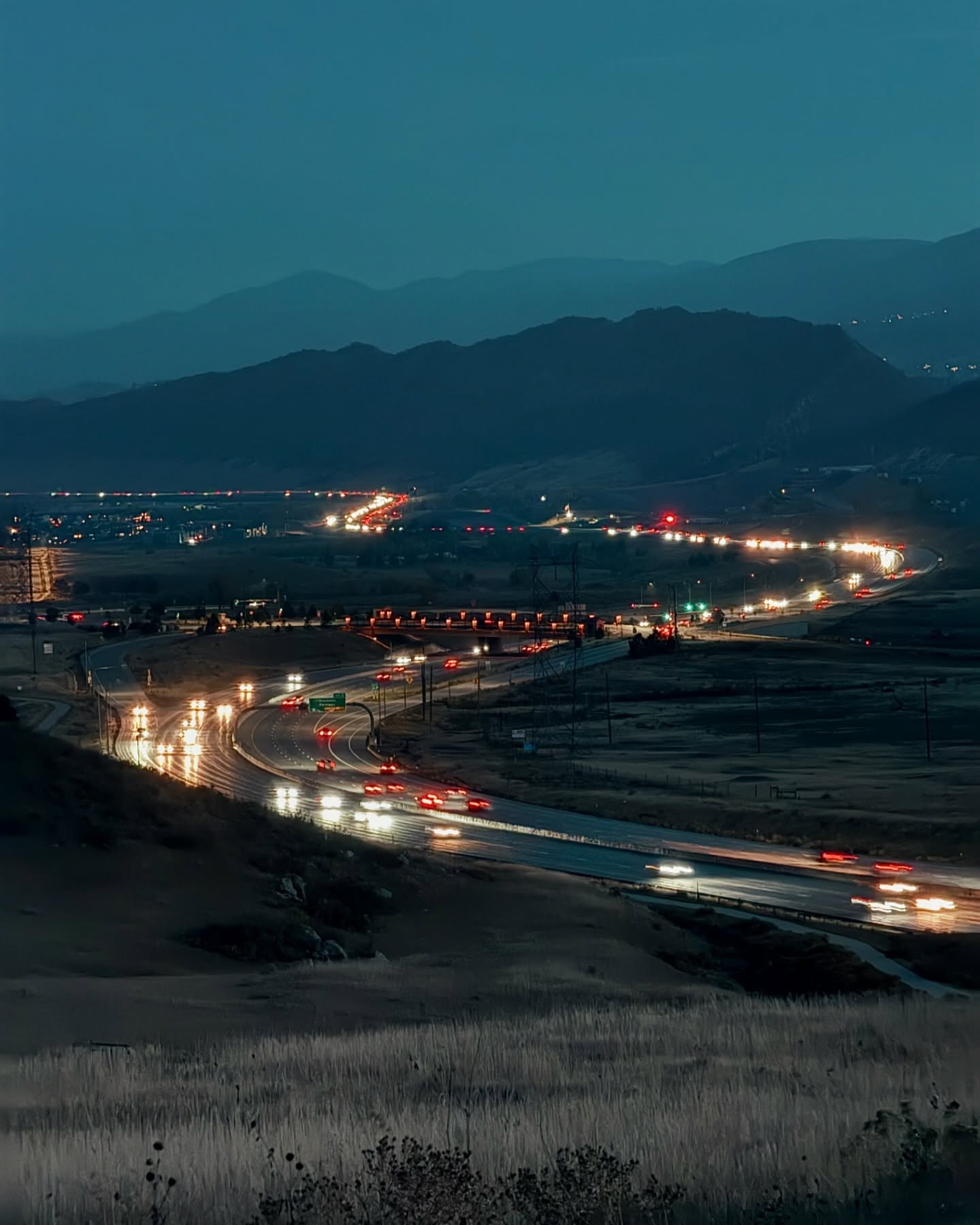 Long-exposure of a Colorado highway at dusk, headlight and taillight trails curving toward the foothills