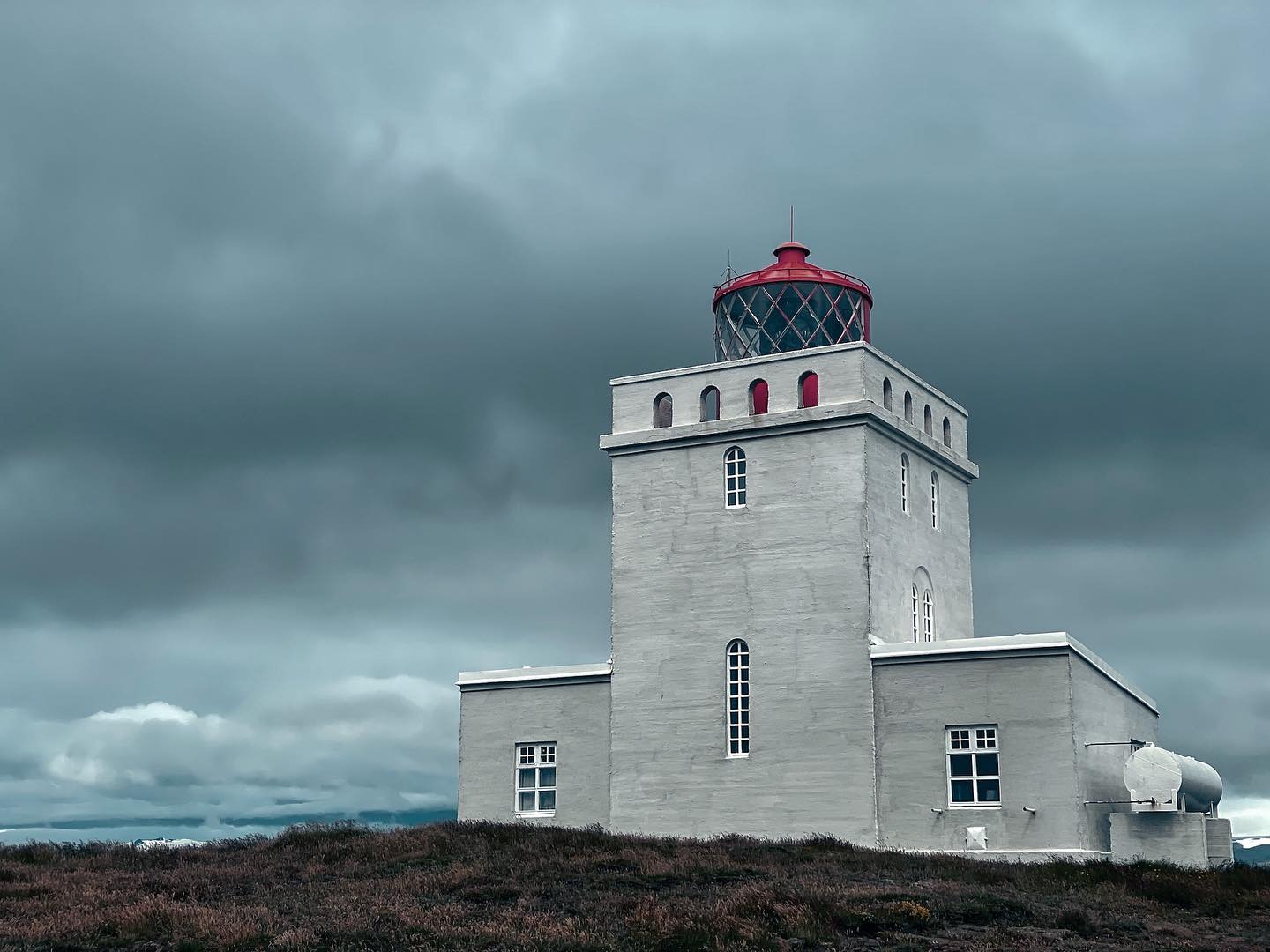 A white lighthouse with a red top against moody storm clouds on the Iceland coast